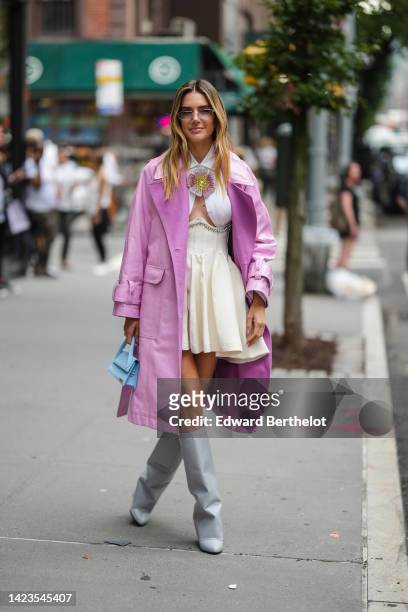Guest wears sunglasses, a pale purple shiny leather long trench coat, a white cropped shirt with embroidered pink / yellow rhinestones flower brooch...