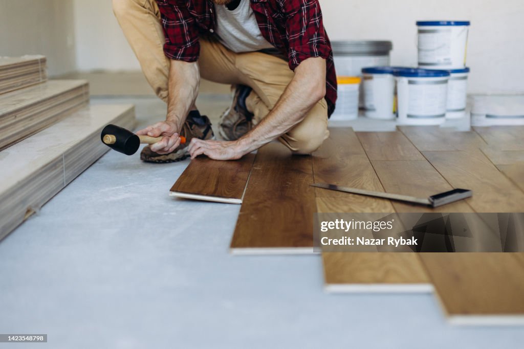 Installing the parquet floor, a man hands fixing one tile with a hammer