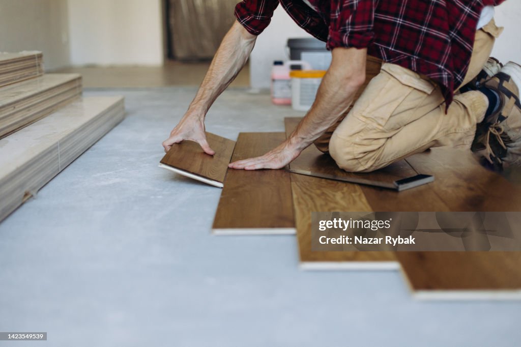 O homem está instalando a tábua de madeira do piso do parquet
