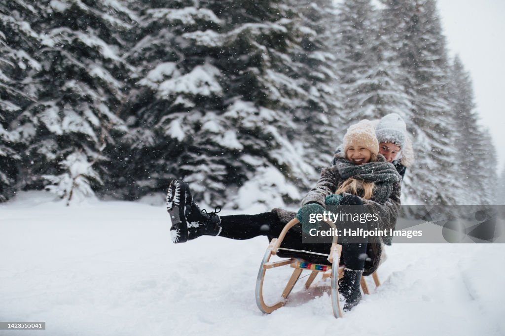 Young couple in love sledding in wintery nature under falling snow.