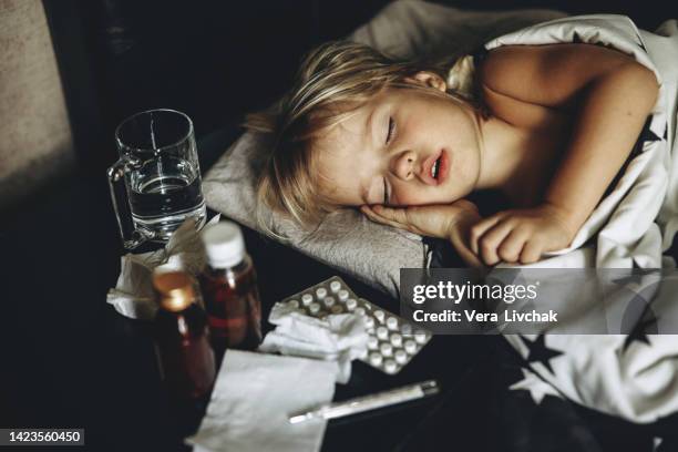 sick toddler is sleeping on a bed attempting to recover from the cold and flu season - boy asleep in bed stock-fotos und bilder