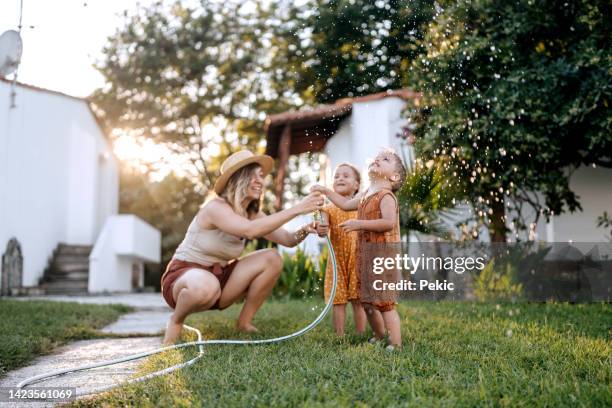 fun times with mother in a backyard - two kids playing with hose stock pictures, royalty-free photos & images