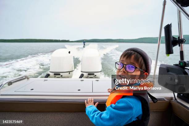 a boy with glasses and a life jacket and a hat on a boat. - asian fishing boat stock-fotos und bilder