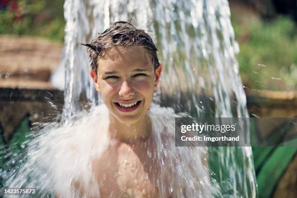 teenage boy enjoying being splashed in waterpark - 13 year old cute boys stock pictures, royalty-free photos & images