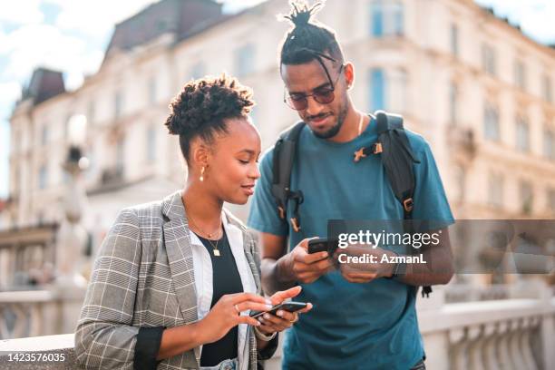 handsome young black couple using smart phones while hanging out in the city - black stock trader stock pictures, royalty-free photos & images