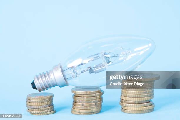 picture representing the increase in electricity bills in times of inflation. light bulb on coins three piles of coins in order from smallest to largest quantity. - energy bill stock pictures, royalty-free photos & images