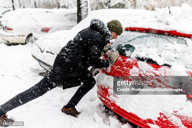 man is pushing a car stuck in snow. - shoveling driveway stock pictures, royalty-free photos & images