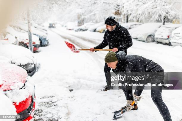 two friends are solving the problems with snow around car using shovels. - snow shovel man stock pictures, royalty-free photos & images