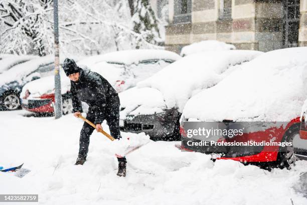 junger mann putzt einen schnee mit schaufel vor einem auto. - schneesturm stock-fotos und bilder