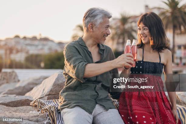 happy couple drinking soda on a date by the beach - asian female friends drinking soda outdoor stock pictures, royalty-free photos & images