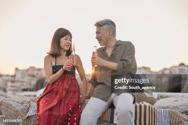 happy couple drinking soda on a date by the beach - japanese couple beach stock pictures, royalty-free photos & images