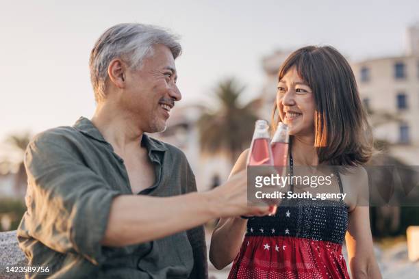 happy couple drinking soda on a date by the beach - asian female friends drinking soda outdoor stockfoto's en -beelden