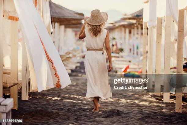 back view of carefree woman walking on the beach. - straw hat stock pictures, royalty-free photos & images