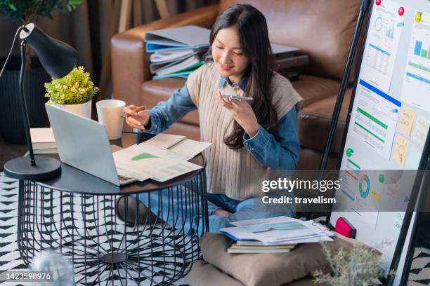 conferencia telefónica a través de teléfono inteligente, mujer adulta asiática que trabaja en casa, hablando con su cliente discutiendo sobre el presupuesto y las ganancias para el nuevo proyecto de la empresa en casa, el trabajo informal se sienta en - competición individual fotografías e imágenes de stock