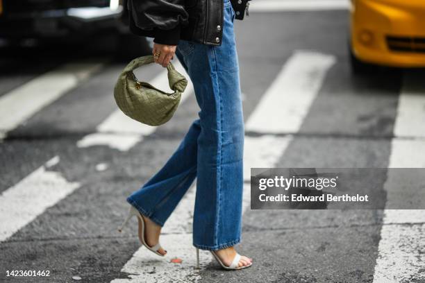 Guest wears a black shiny leather oversized jacket, blue denim straight pants, a khaki shiny leather braided Jodie handbag from Bottega Veneta, gold...