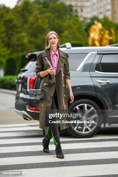 Guest wears a white and pink striped print pattern shirt, a khaki long buttoned trench coat from Burberry, a gray shiny leather East-West handbag,...