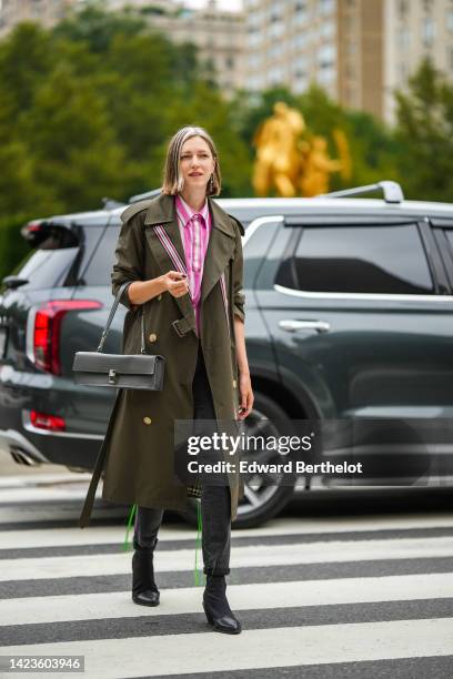 Guest wears a white and pink striped print pattern shirt, a khaki long buttoned trench coat from Burberry, a gray shiny leather East-West handbag,...