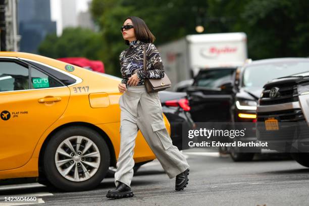 Guest wears black sunglasses, a dark brown / beige / navy blue print pattern long sleeves t-shirt, a Juste Un Clou ring from Cartier, a gold Clash...