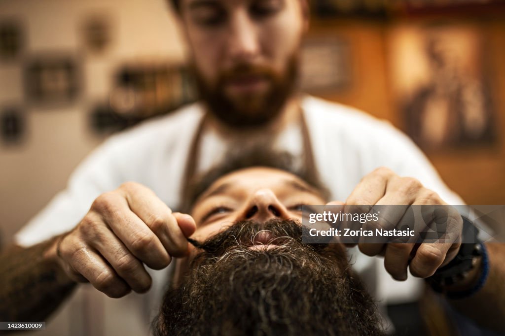 Barber styling mustaches of a customer in barber shop