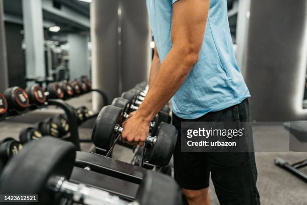 young man picking a dumbbell at the gym - man choosing stock pictures, royalty-free photos & images
