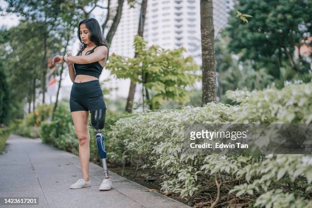 Asian female athlete with disability checking her heart beat electrocardiography with fitness tracker pedestrian walkway after jogging in. the morning