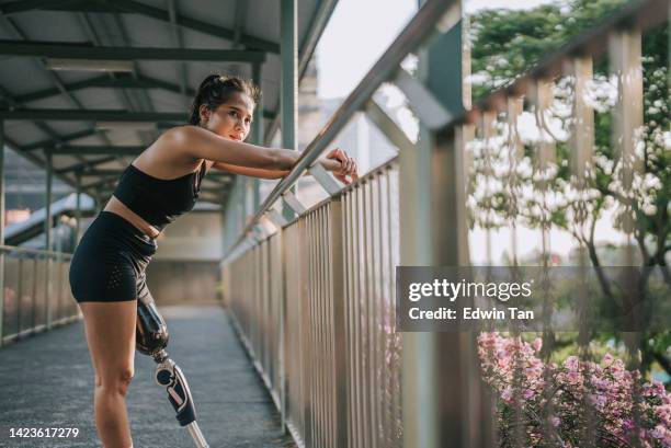 asian female athlete with disability artificial leg resting leaning at footbridge after jogging in the morning - disabled sportsperson stock pictures, royalty-free photos & images