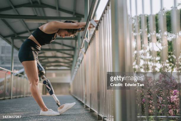 atleta asiática con discapacidad calentamiento artificial de piernas estirando en el puente peatonal antes de trotar por la mañana - equipo protésico fotografías e imágenes de stock