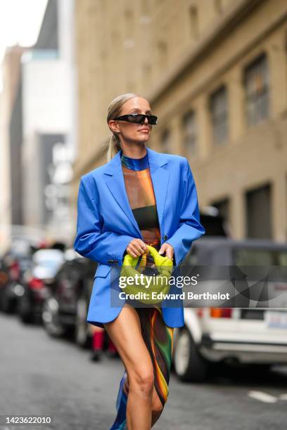 Leonie Hanne wears black square sunglasses, a royal blue oversized blazer jacket, navy blue / flashy blue / yellow / green print pattern long...