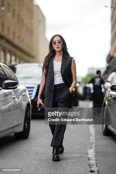 Chriselle Lim wears black sunglasses, silver sunglasses, a black sleeveless long blazer jacket, a beige tank-top, black large pants, black shiny...