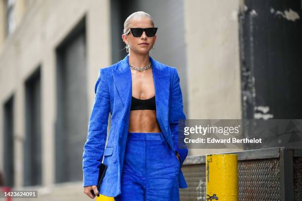 Caroline Daur wears black sunglasses, large silver chain earrings, a matching large silver chain necklace, a rhinestones necklace, a royal blue...