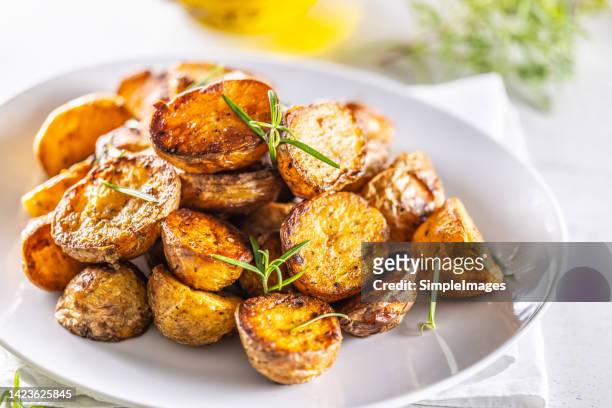 golden baked potatoes on a white plate with rosemary. - roast potatoes stock pictures, royalty-free photos & images
