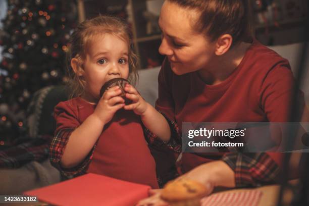 cute little girl looking at camera as she is taking a bite out of a chocolate muffin - chocolate muffin eating stock pictures, royalty-free photos & images