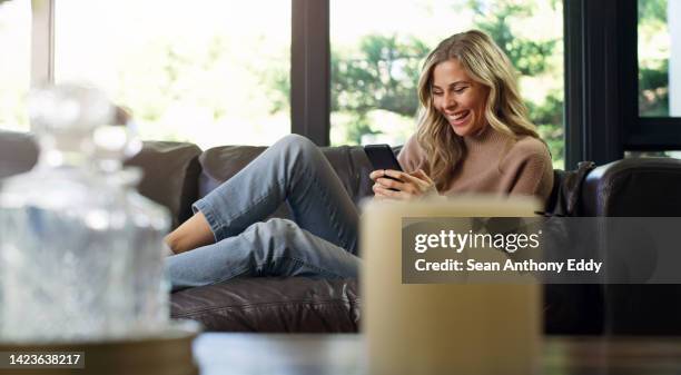 woman on a sofa, with a phone and a smile on social media or texting friends and family. relax, smile and be happy, online shopping or internet surfing, beautiful girl on couch in luxury living room. - modern family media call stockfoto's en -beelden