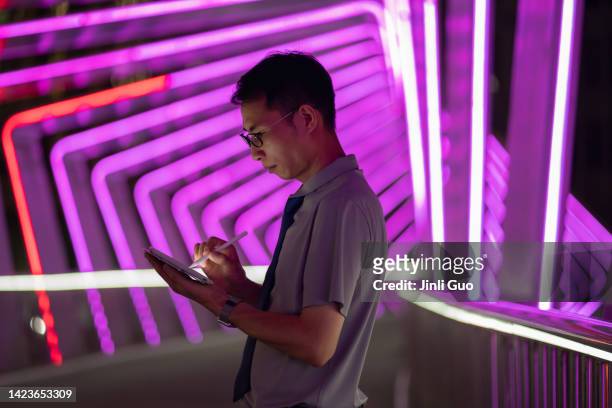 mann, der einen digitalen stift hält und ein tablet auf lila neonlichthintergrund verwendet - digitized pen stock-fotos und bilder
