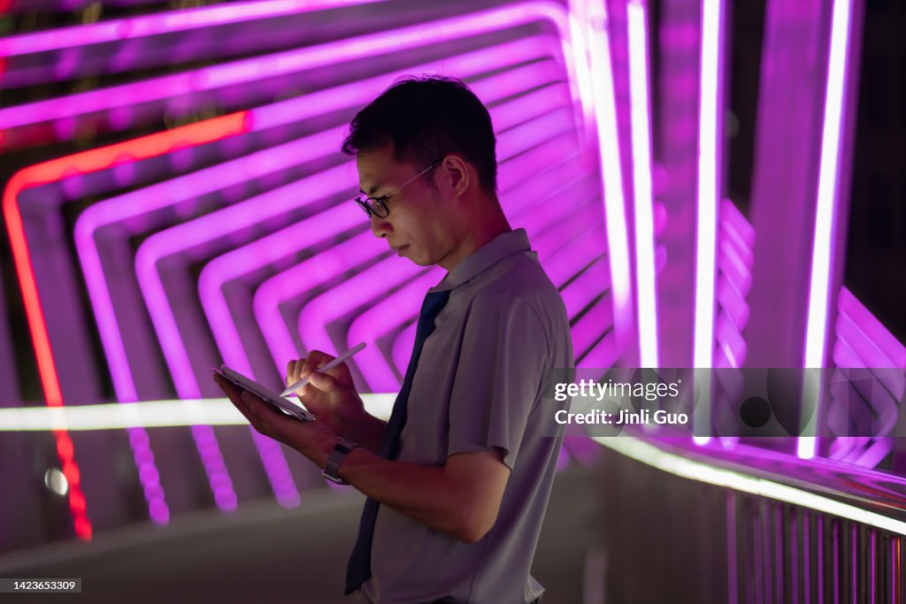Man holding digital pen and using tablet on purple neon light background