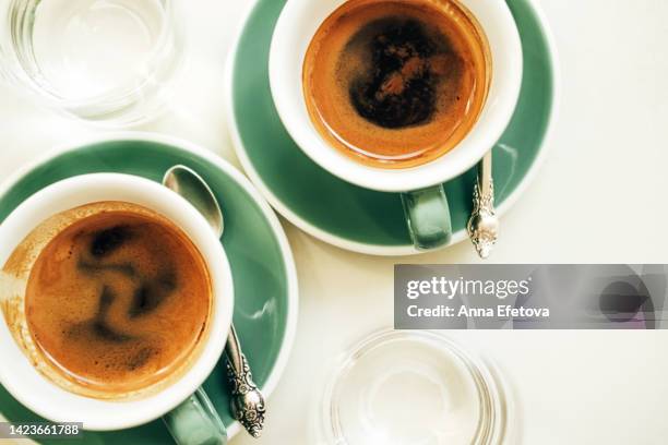 coffee break with a friend. two green ceramic cups of americano and glass cups of water placed on white table. photography from above - crema stock pictures, royalty-free photos & images