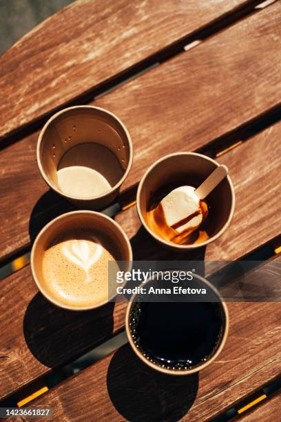 coffee break with friends. four disposable cups with water, cappuccino, brewed coffee and coffee with ice cream placed on wooden table. photography from above with copy space for your design - takeaway coffee cup stock pictures, royalty-free photos & images