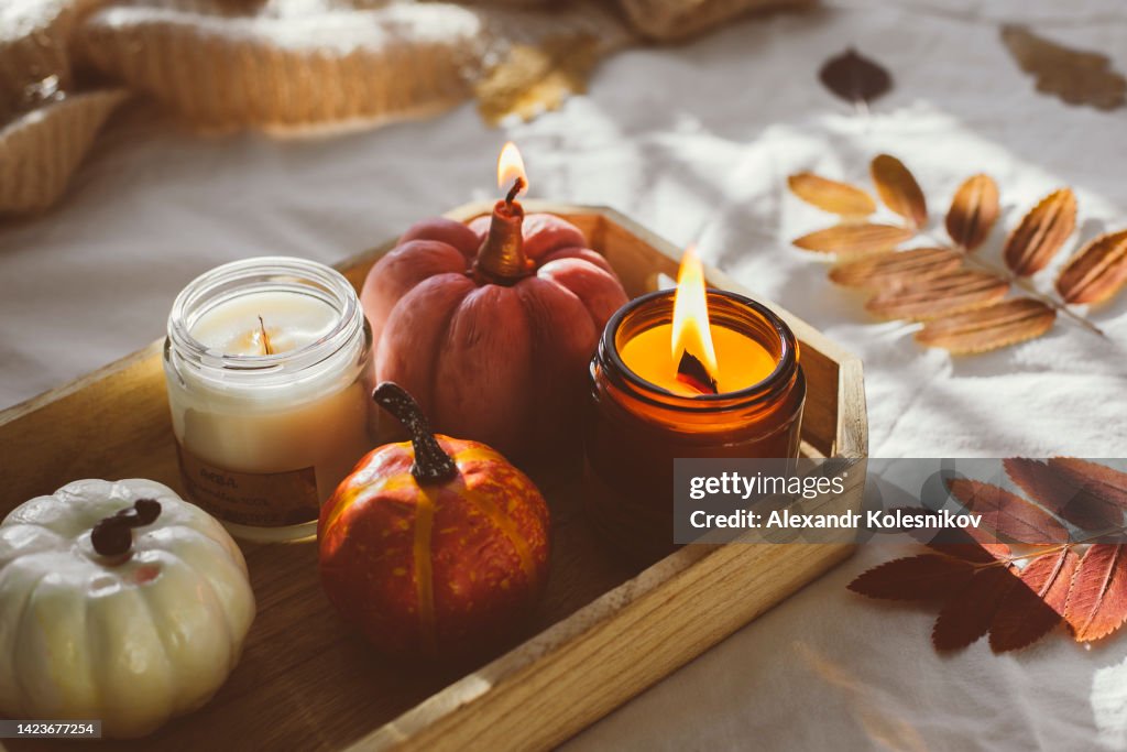 Wooden tray with atmospheric candles and aututmn fall leaves on white bed.