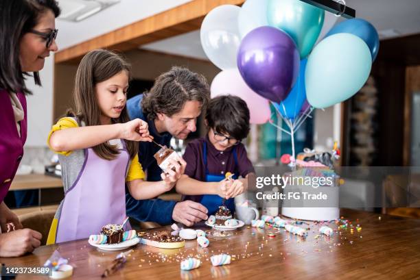 siblings opening and playing with sweets on a children's present with parents at home - cupcake box stock pictures, royalty-free photos & images