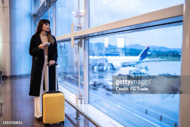 contemplative young woman using mobile phone in the airport - project traveller stock pictures, royalty-free photos & images