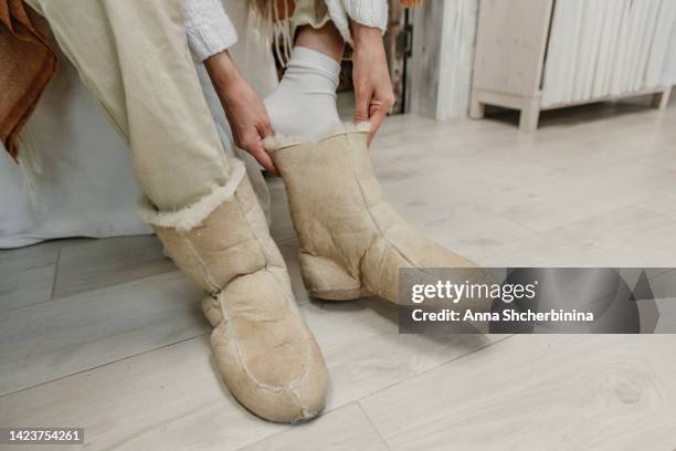 a woman in a sweater and beige pants puts on warm ugg boots. close-up. it's cold in the house. life in conditions of saving heat energy. - ugg boot stock pictures, royalty-free photos & images