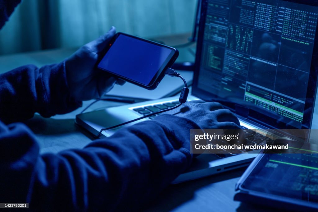 Hacker with mobile phone and computer in a dark room. Cyber crime concept.