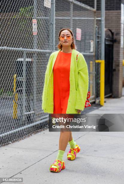 Guest wearing yellow cardigan, orange dress, socks, sandals outside Cos on September 13, 2022 in New York City.