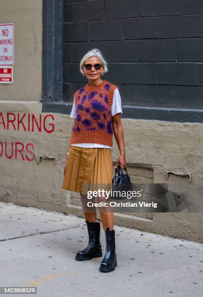 Grece Ghanem wearing pull under, beige pleated shirt, white shirt, black bag, boots outside Cos on September 13, 2022 in New York City.