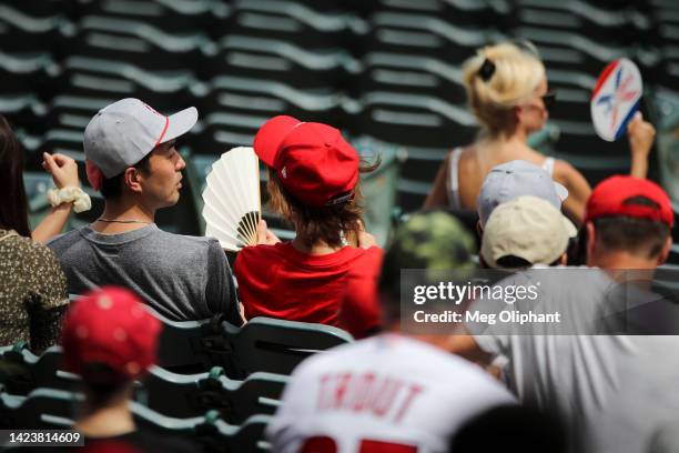 People fan themselves during extreme heat conditions ahead of the game between the Los Angeles Angels and the Houston Astros at Angel Stadium of...