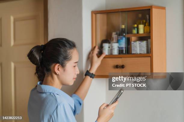 a woman is looking for medicine in the medicine cabinet at home. - acetylsalicylizuur stockfoto's en -beelden