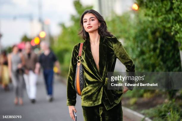 Guest wears gold pendant with embroidered diamonds earrings, a green shiny velvet belted jacket, matching green shiny velvet large pants, a beige and...