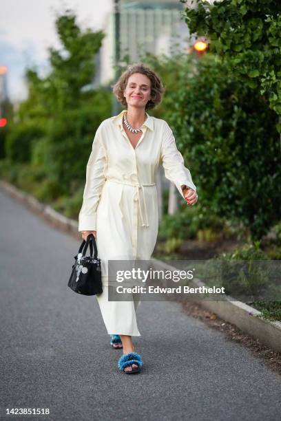 Guest wears earrings, a gold large wavy necklace, a pale yellow long shirt, a black suede with embroidered large sequined handbag, blue glitter...