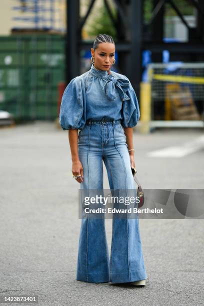 Guest wears gold earrings, a blue denim faded short puffy sleeves / high knot neck / cropped top, matching blue faded denim large flared pants, a...
