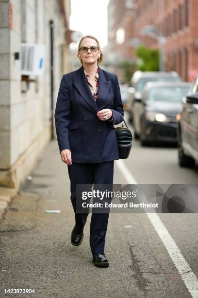 Guest wears black sunglasses, diamonds flower earrings, a beige / navy blue / red / brown print pattern silk shirt, a deep navy blue blazer jacket,...